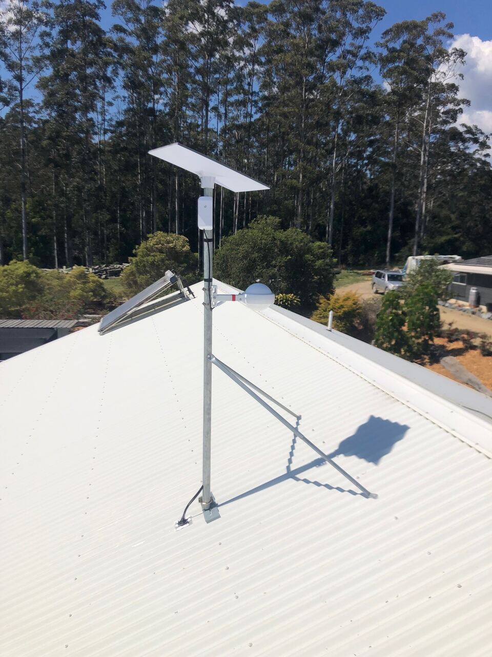 A Starlink dish on a tall pole mount at the roof ridge, with a point-to-point WiFi bridge on the same pole